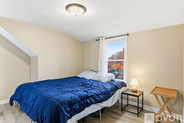 A bedroom with a blue bedspread and a window showing a tree with autumn leaves.