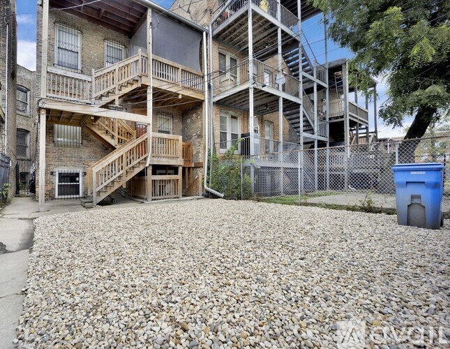 A gravel courtyard in front of a multi-story building with a blue dumpster.
