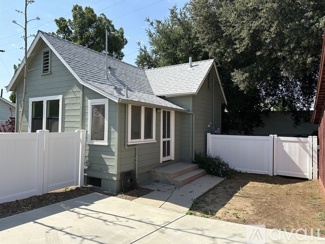 A small house with a grey roof and white fence.