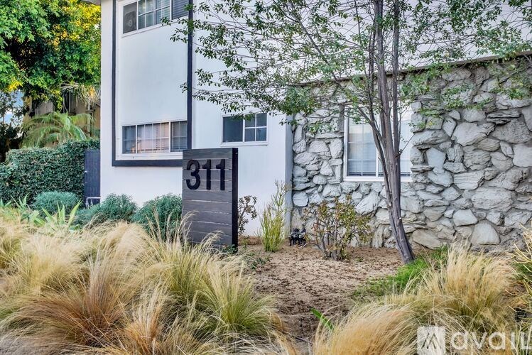 A stone wall and a tree are in front of a building with a number 311 on it.