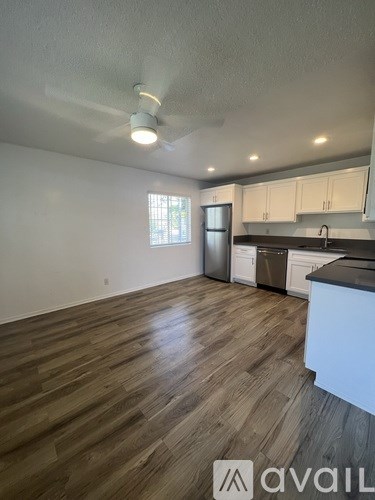 A room with wooden flooring and a kitchen area with white cabinets.
