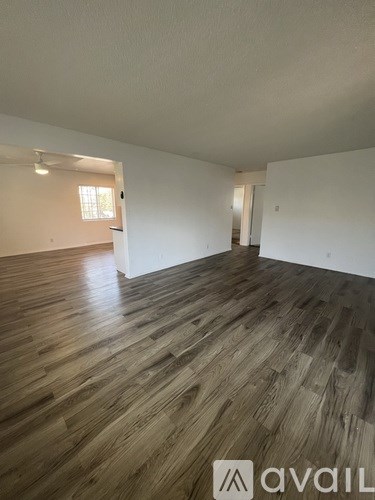 A room with wooden flooring and white walls, with a window on the left wall.