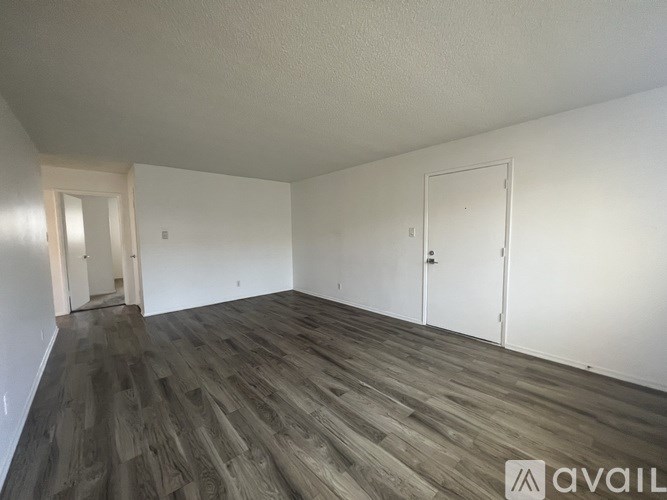 A room with wooden flooring and white walls, with a door on the right side.
