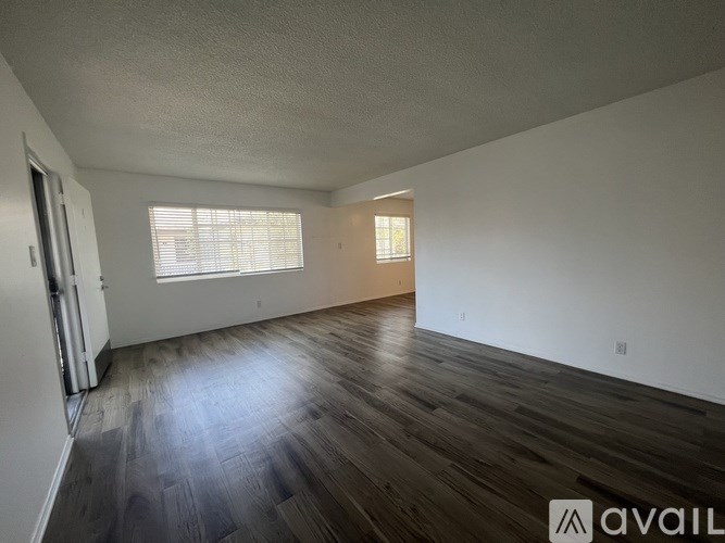 A spacious room with wooden flooring and a window with blinds.