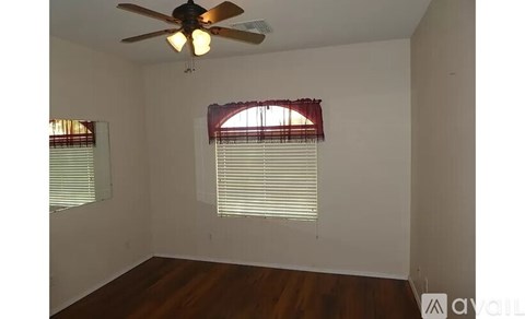 A room with a ceiling fan and two windows with blinds.