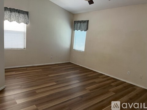 A room with wooden flooring and two windows with curtains.