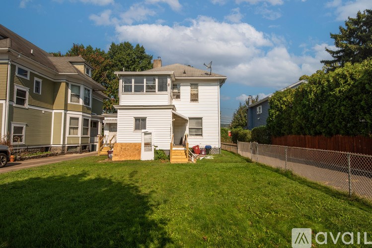 A white house with a brown roof is surrounded by a green lawn and other houses.