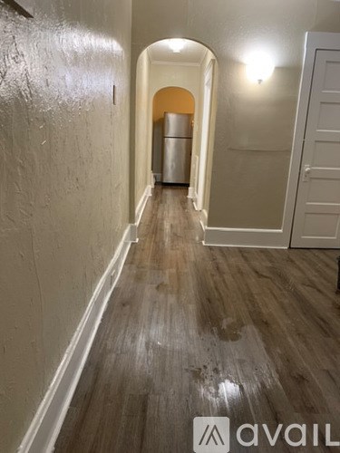 A hallway with a wooden floor and white walls leading to a kitchen.