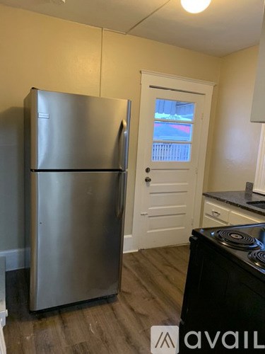 A stainless steel refrigerator stands in a kitchen with a white door.