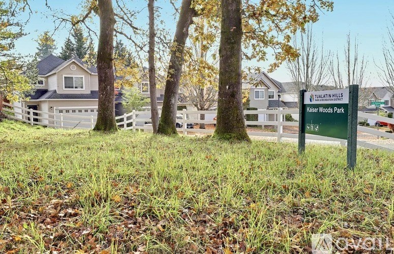 A sign for Kasser Woods Park stands in a grassy area with trees and houses in the background.