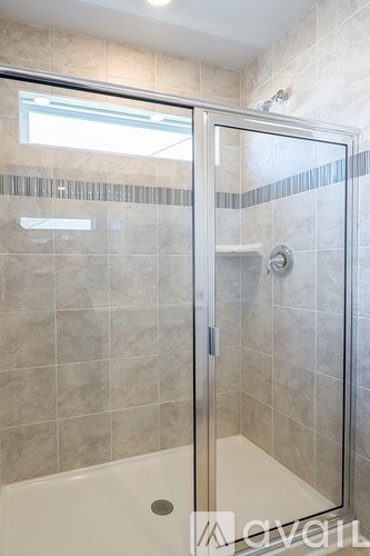 A shower with a glass door and a tiled wall.