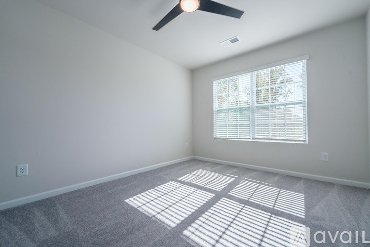A room with a fan, carpet, and a window with blinds.
