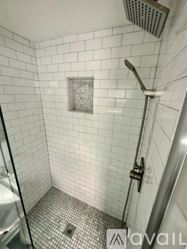 A white tiled bathroom with a shower head and a drain.