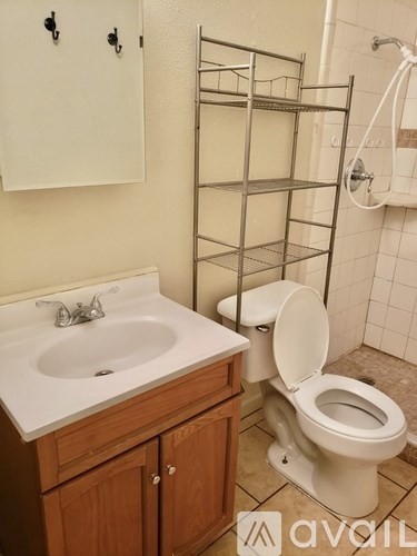 A white toilet is in a bathroom with a sink and a rack.