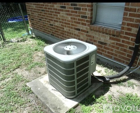 An air conditioner unit is placed on a concrete slab outside a brick building.