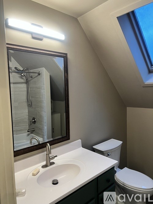 A bathroom with a toilet, sink, mirror and a skylight.