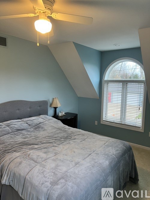 A bedroom with a bed, a nightstand with a lamp, and a window with blinds.