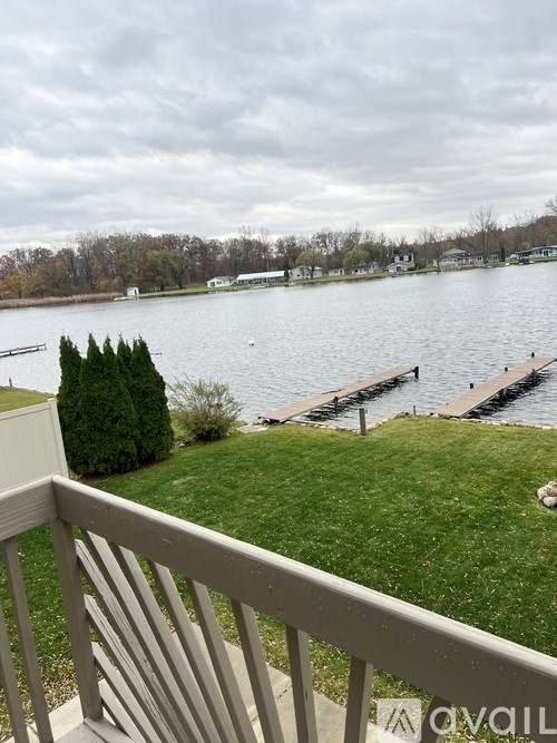 A view from a balcony overlooking a lake with a dock and trees in the distance.