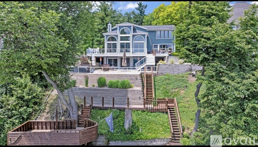 A large house with a deck and a hot tub is surrounded by trees.