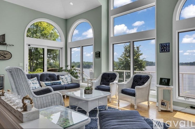 A living room with a white sofa and chairs, a glass table, and a view of Lake Como through the windows.