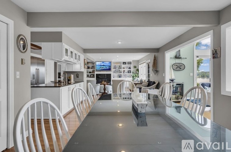 A modern kitchen with white chairs and a long table.