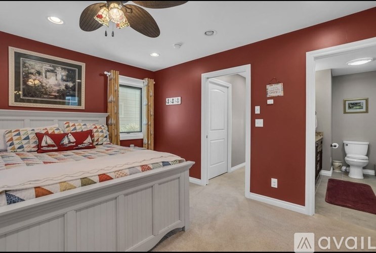 A bedroom with a bed, a ceiling fan, and a bathroom visible in the background.