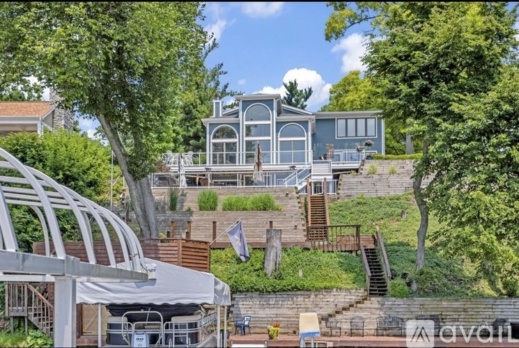 A modern house with a curved roof and a glass wall is surrounded by greenery.