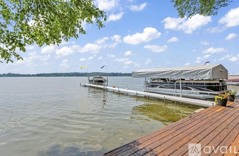 A wooden dock extends into a lake with a boat house and a flag on it.