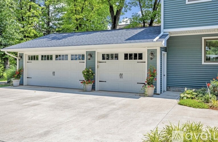 A two-car garage with a blue house and greenery in the background.