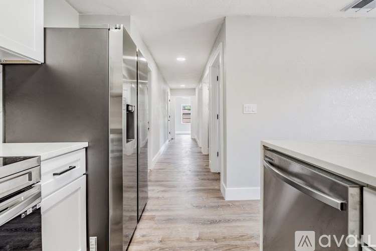 A long, narrow, white hallway with a stainless steel refrigerator on the left.