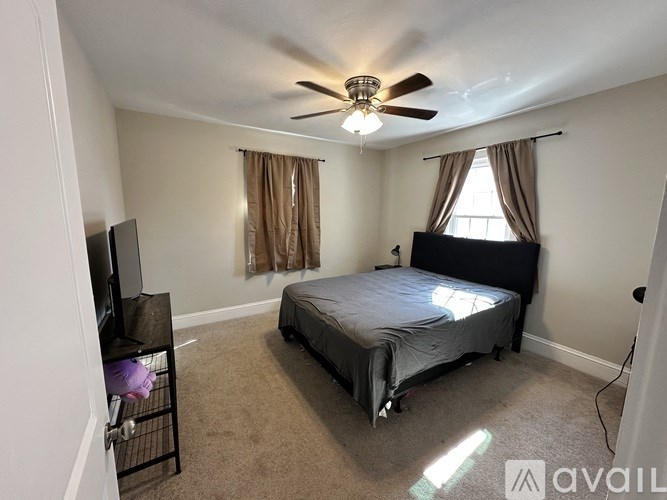A bedroom with a bed, a television, and a ceiling fan.