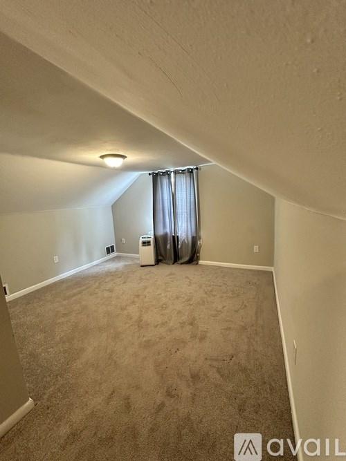 A room with carpeted floor and a window with curtains.