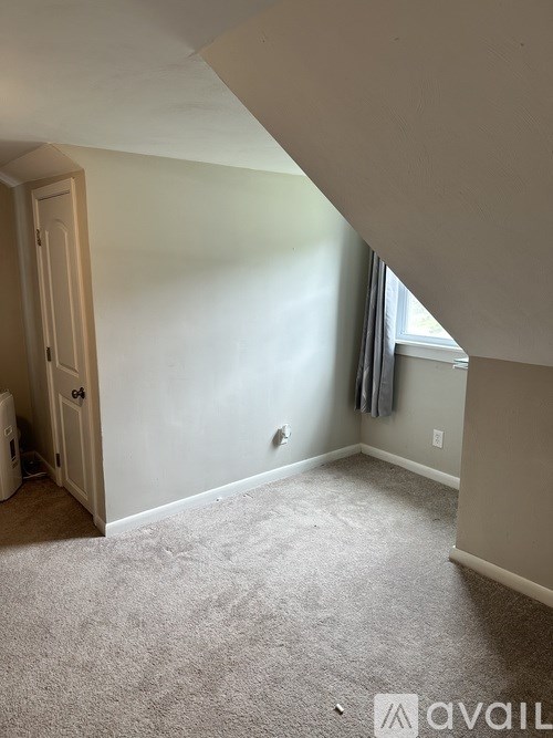 A room with a carpeted floor and a window with a curtain.
