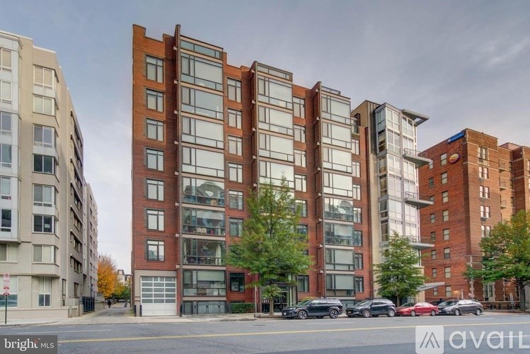 A tall building with many windows is in the middle of a street with cars parked on the side.
