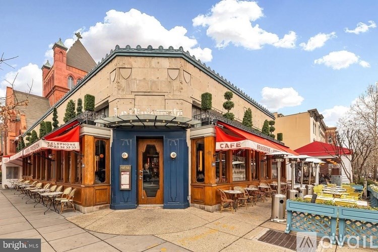 A cafe with a blue door and red awnings is surrounded by trees and other buildings.