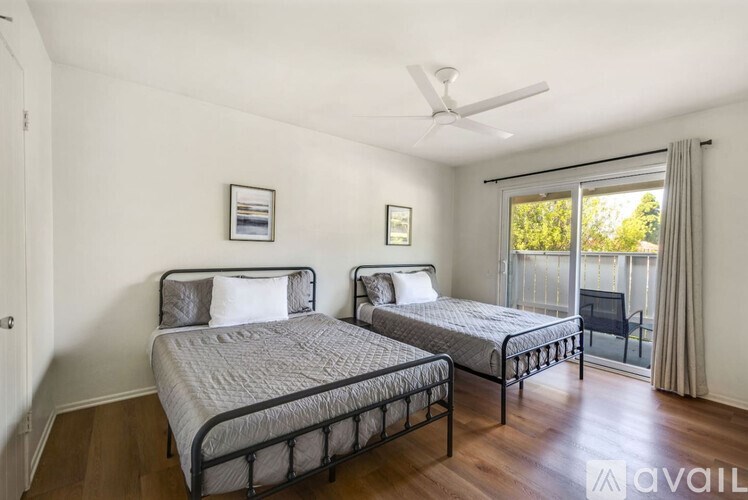 Two twin beds in a room with a ceiling fan and sliding glass doors.