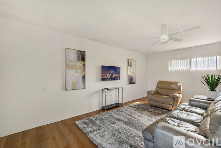 A living room with a grey rug, a beige sofa, a chair, a small table and a ceiling fan.