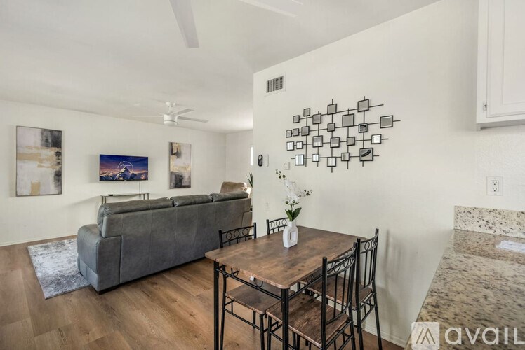 A living room with a grey couch, a wooden table with four chairs, and a wall with a series of black and white square pictures.