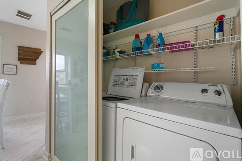 A white washing machine is in a laundry room with a glass door.