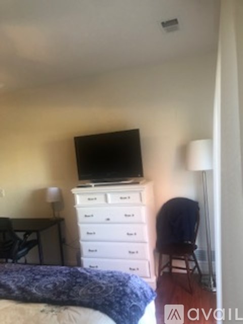 A bedroom with a bed, a dresser with a television on top, a chair, and a desk.