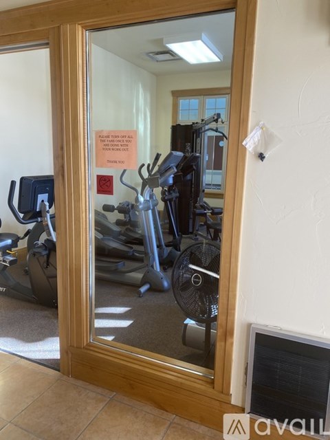 A mirror reflects a room with a treadmill and a fan.