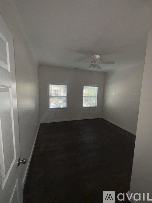 A room with a ceiling fan and two windows.