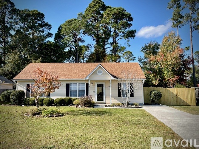 A small house with a brown roof and a white door is surrounded by a grassy lawn and a wooden fence.
