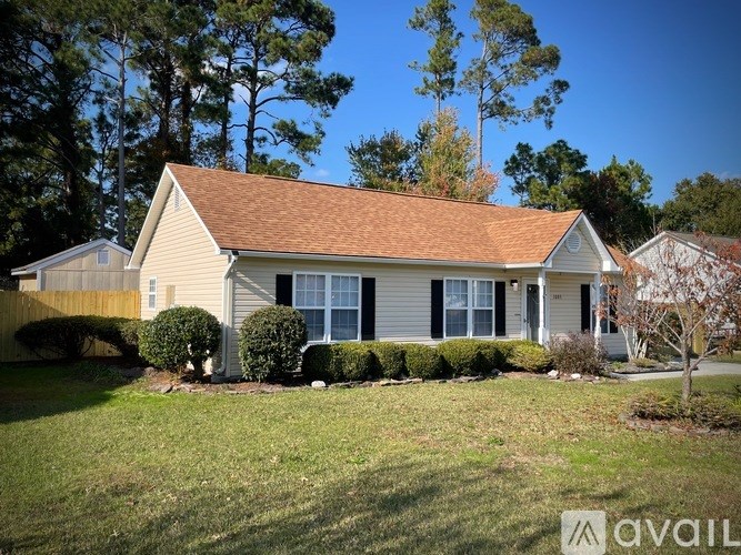 A house with a brown roof and white siding is surrounded by a grassy lawn and trees.