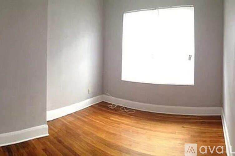 A room with wooden flooring and a window letting in sunlight.