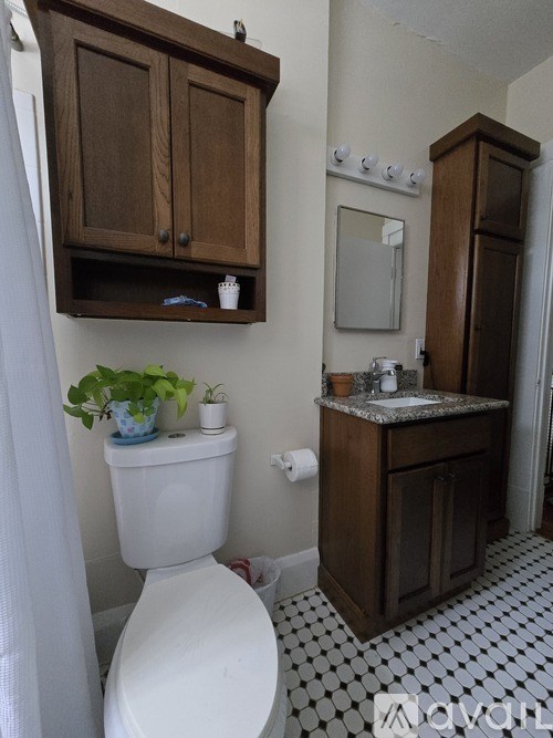 A white toilet sits under a wooden cabinet in a bathroom.