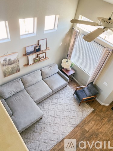 A living room with a grey couch and a fan.