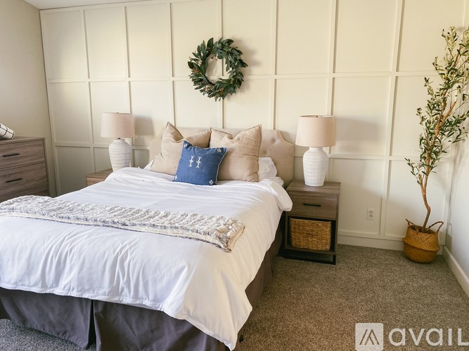 A bedroom with a large bed, two lamps, a wreath, and a plant.