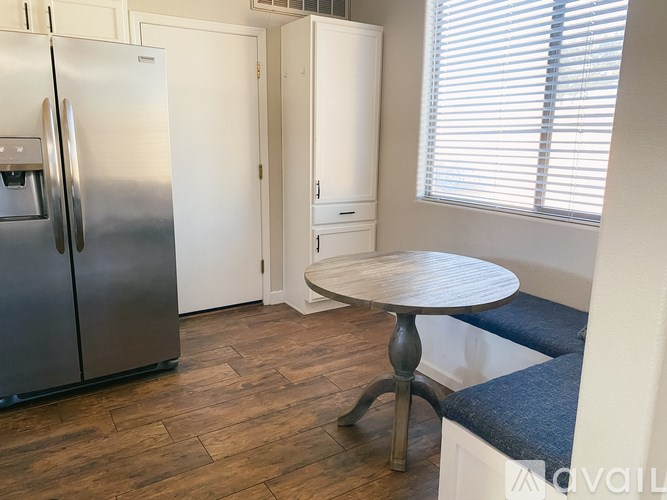 A kitchen with a refrigerator, a table, and a bench.