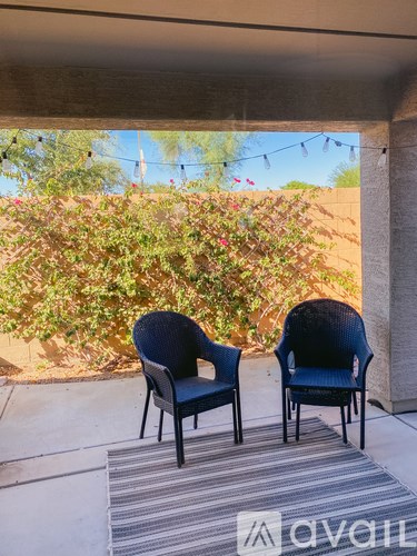 Two black chairs are placed on a patio with a striped rug in front of them.